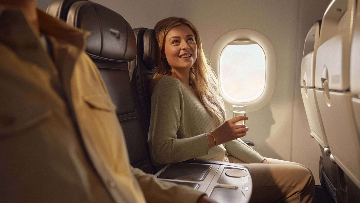 A female passenger sat in a Club Europe window seat with a drink.