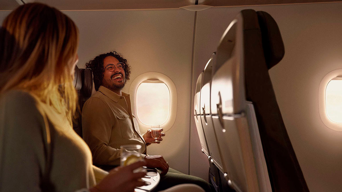 A male passenger sat in a Club Europe cabin, laughing while holding a drink next to a female passenger.