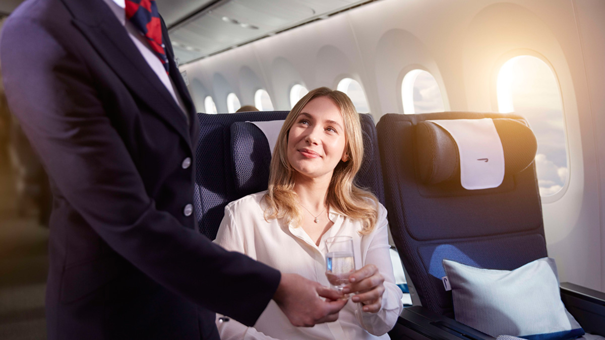 Woman sitting in premium economy World Traveller Plus with drink. 