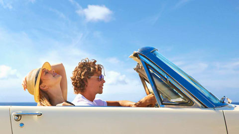 Couple driving convertible under blue sky.