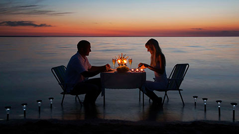 Young couple share a romantic dinner with candles on beach.